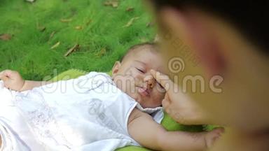 可爱的宝宝慢动作地对妈妈微笑，闭上眼睛。 梦想的新生婴儿躺在户外草地上。 婴儿婴儿婴儿